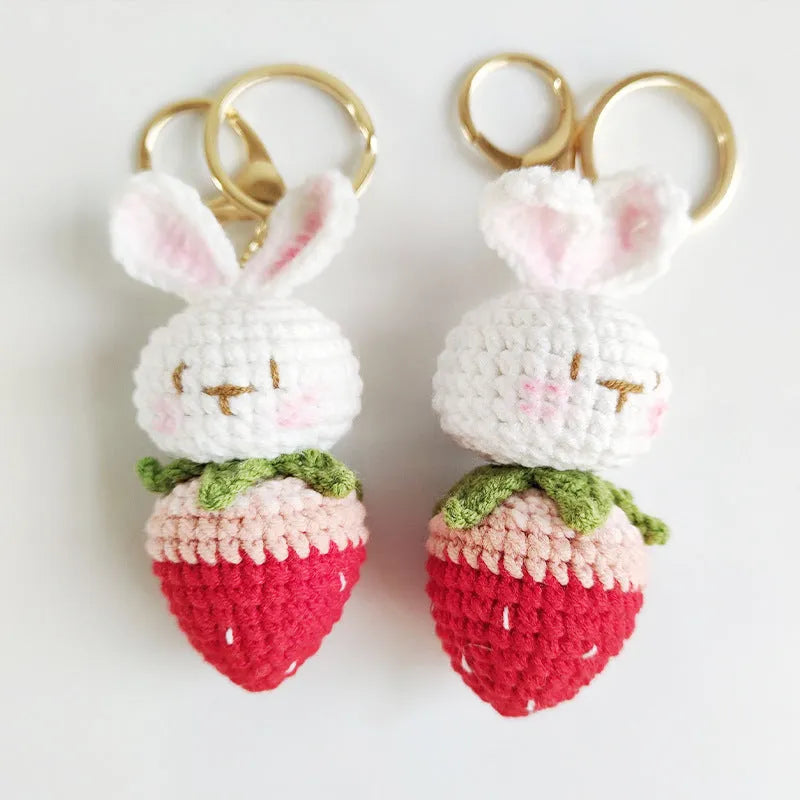 Close-up of a white hand-woven wire pendant showing a rabbit and strawberry cartoon design on a key ring.