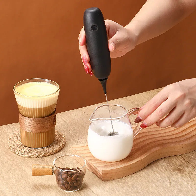 Black and white hand-held electric milk frother and blender on a kitchen counter.