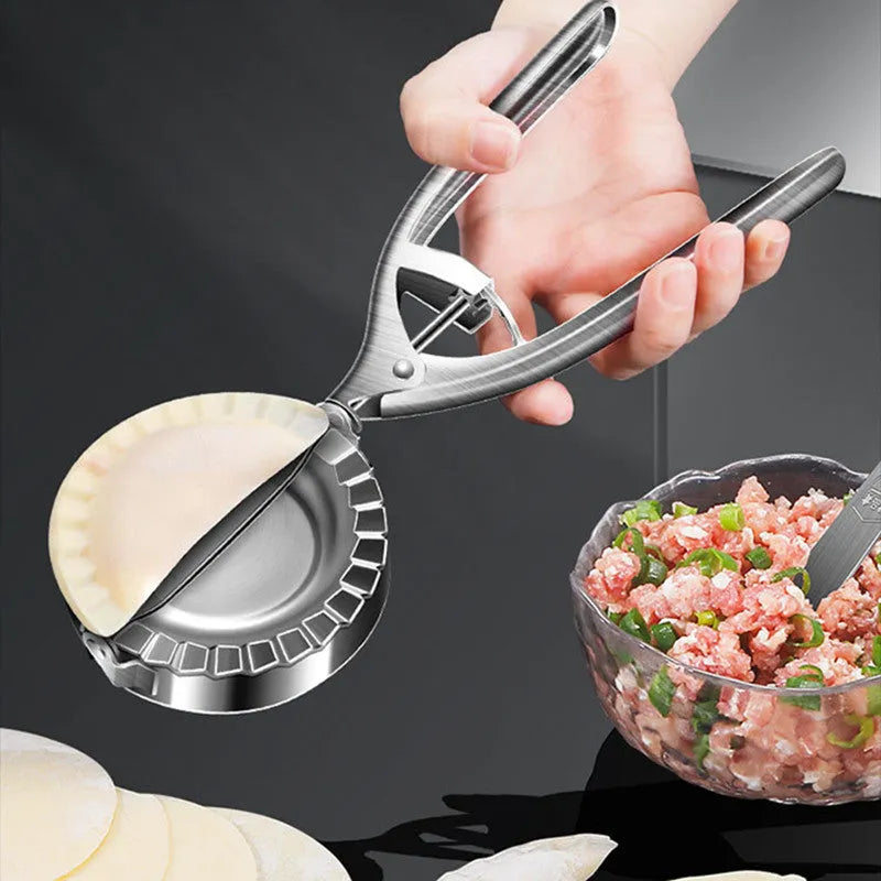 Silver stainless steel manual dumpling maker press tool on a kitchen surface.