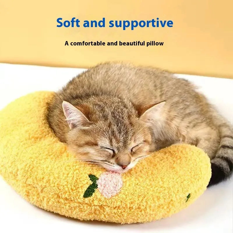Blue U-shaped cloth pet pillow in a question mark shape on a wooden floor next to a cat carrier.