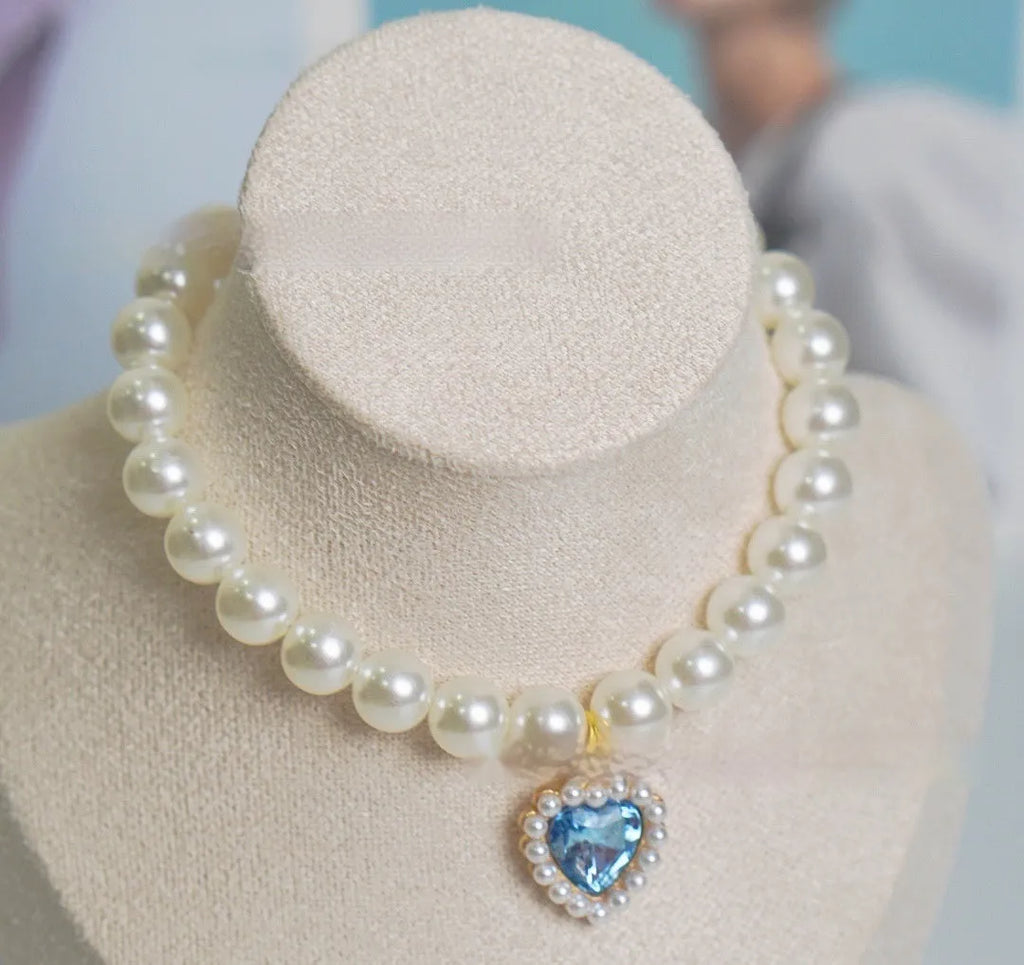 Pearl necklace cat collar with heart-shaped gem charm in various colours on a white background.
