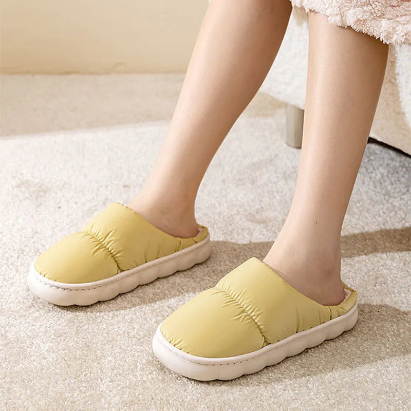 A pair of blue down cotton winter slippers with a thick rubber sole and plush lining on a wooden floor.