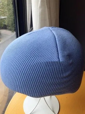 White snow helmet decorative cover with matching beanie hat laid flat on a blue background.