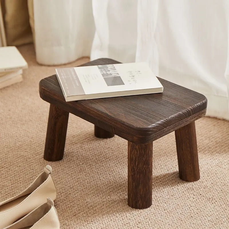 Distressed solid wood household stool for changing shoes in a living room setting.