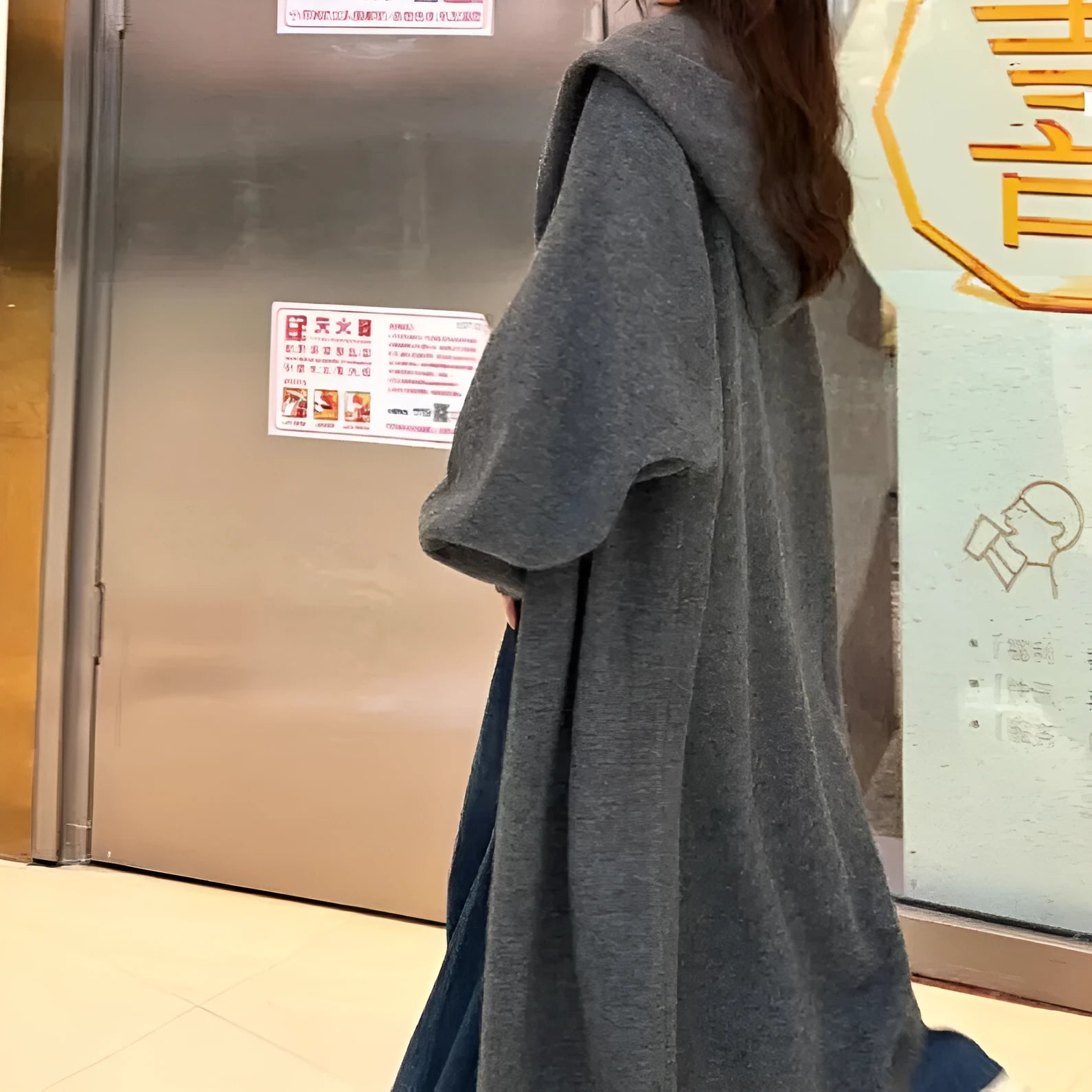 Long beige hooded knitted cardigan on a woman, showcasing its below-the-knee length and loose fit.