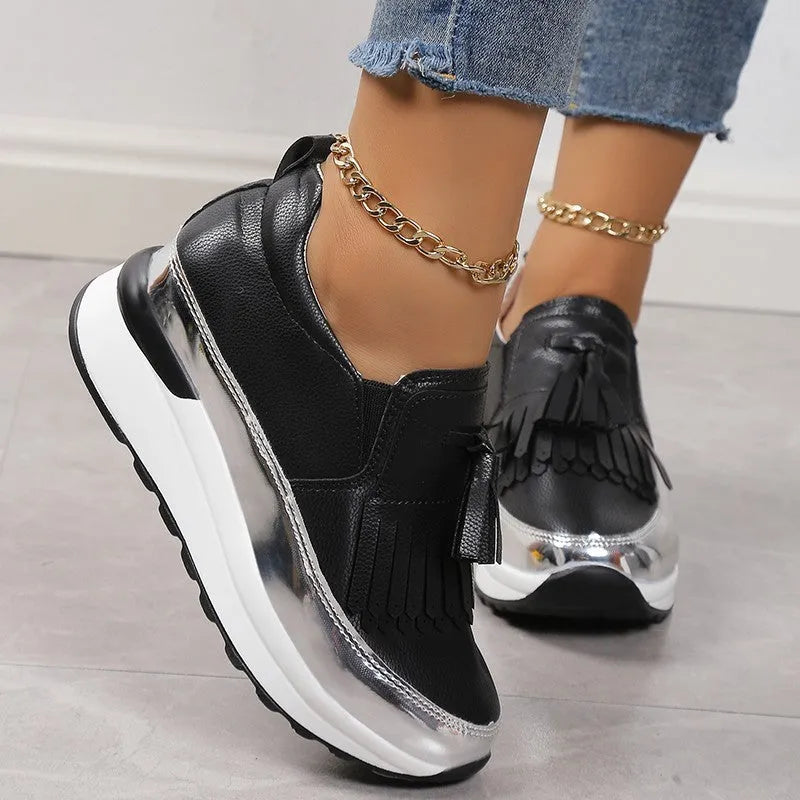 Women's black platform loafers with a tassel detail and a low wedge heel on a white background.