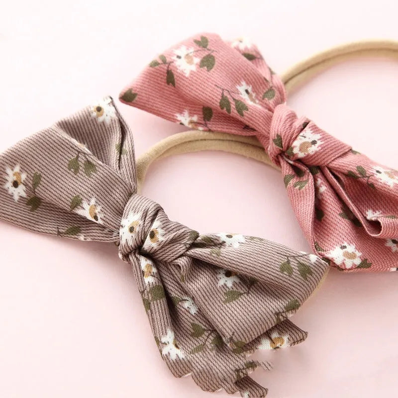 Children's cloth hair band with a white knotted bow, shown against a colour swatch background.