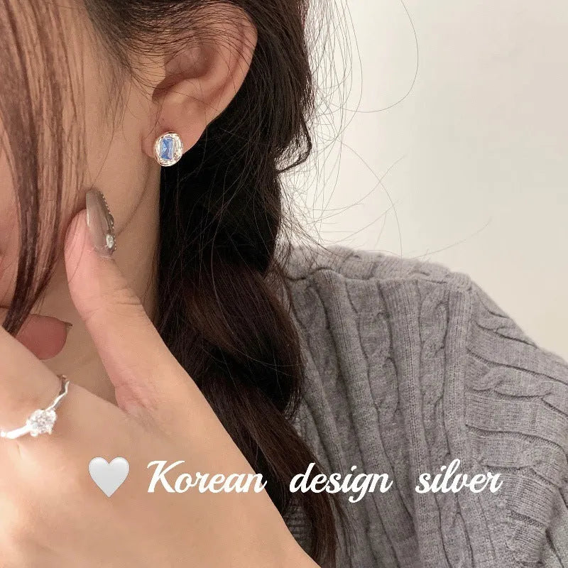 Women's sterling silver earrings with oval heart-wrapped design and blue diamond accents
