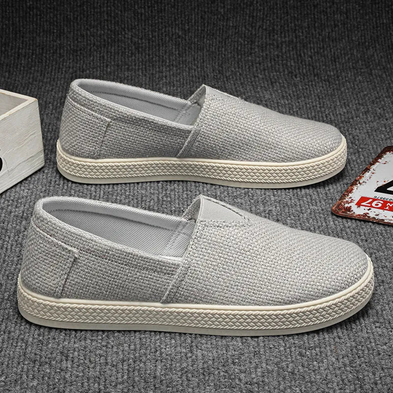 Men's beige linen cloth slip-on shoes with a round toe and shallow mouth on a grey background.