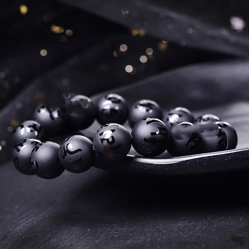 Close-up of a frosted black agate bracelet with Sanskrit mantra engraving on each bead, showing matte stone texture.