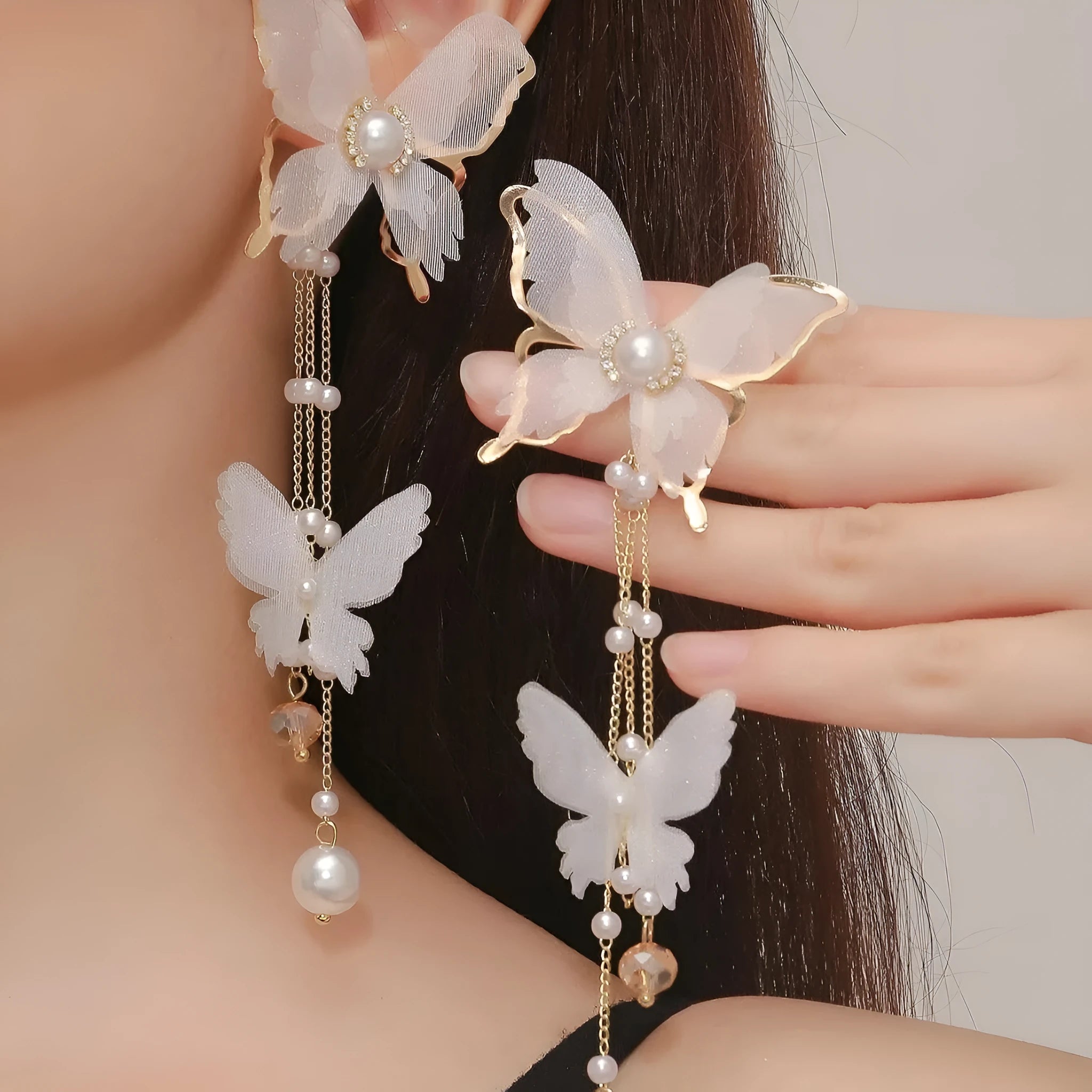 White butterfly-shaped earrings with pearls, rhinestones, and a tassel drop on a model's ear.