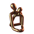 Modern minimalist resin statue of a couple in milky white or gold finish on a wooden surface.