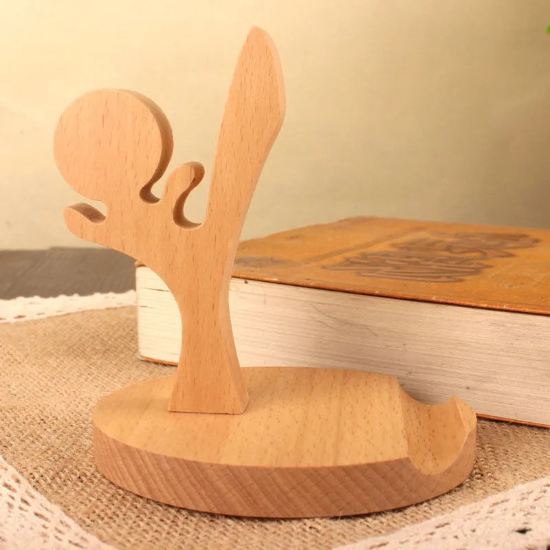 Solid beech wood mobile phone stand with a resin cow figurine and a slot for holding coins on a wooden desk.