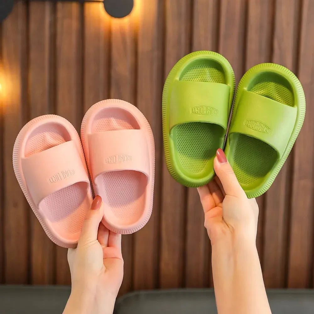 Bright coloured EVA children's house slippers with thick, textured non-slip soles on a wooden floor.