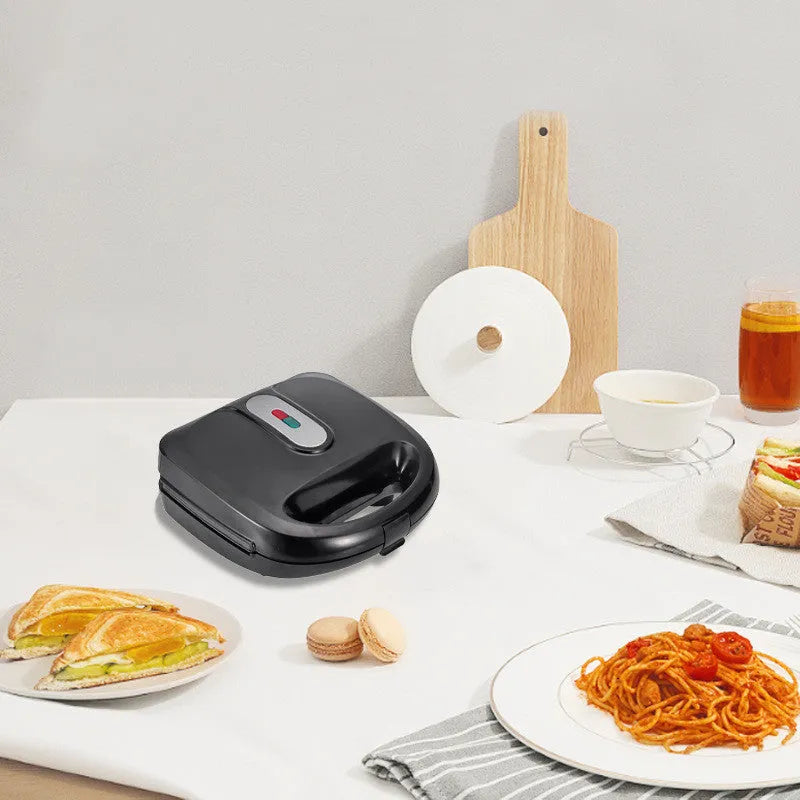 Black electric sandwich pan with brushed stainless steel lid and six non-stick cooking plates on a kitchen counter.