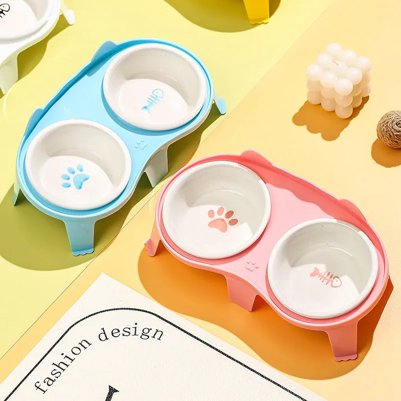 Blue ceramic cat food and water bowl set on a white stand with a hook, showing tilted feeding angle.