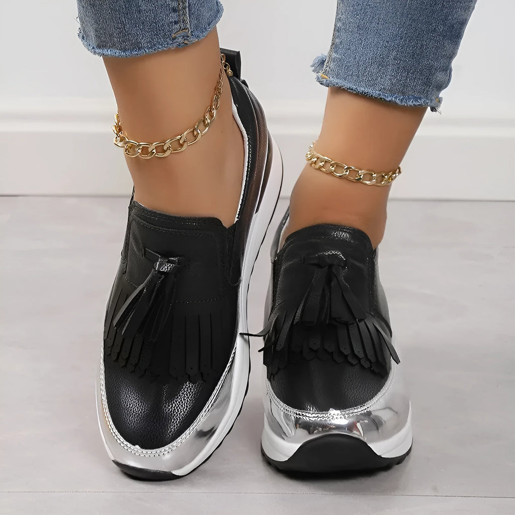 Women's black platform loafers with a tassel detail and a low wedge heel on a white background.
