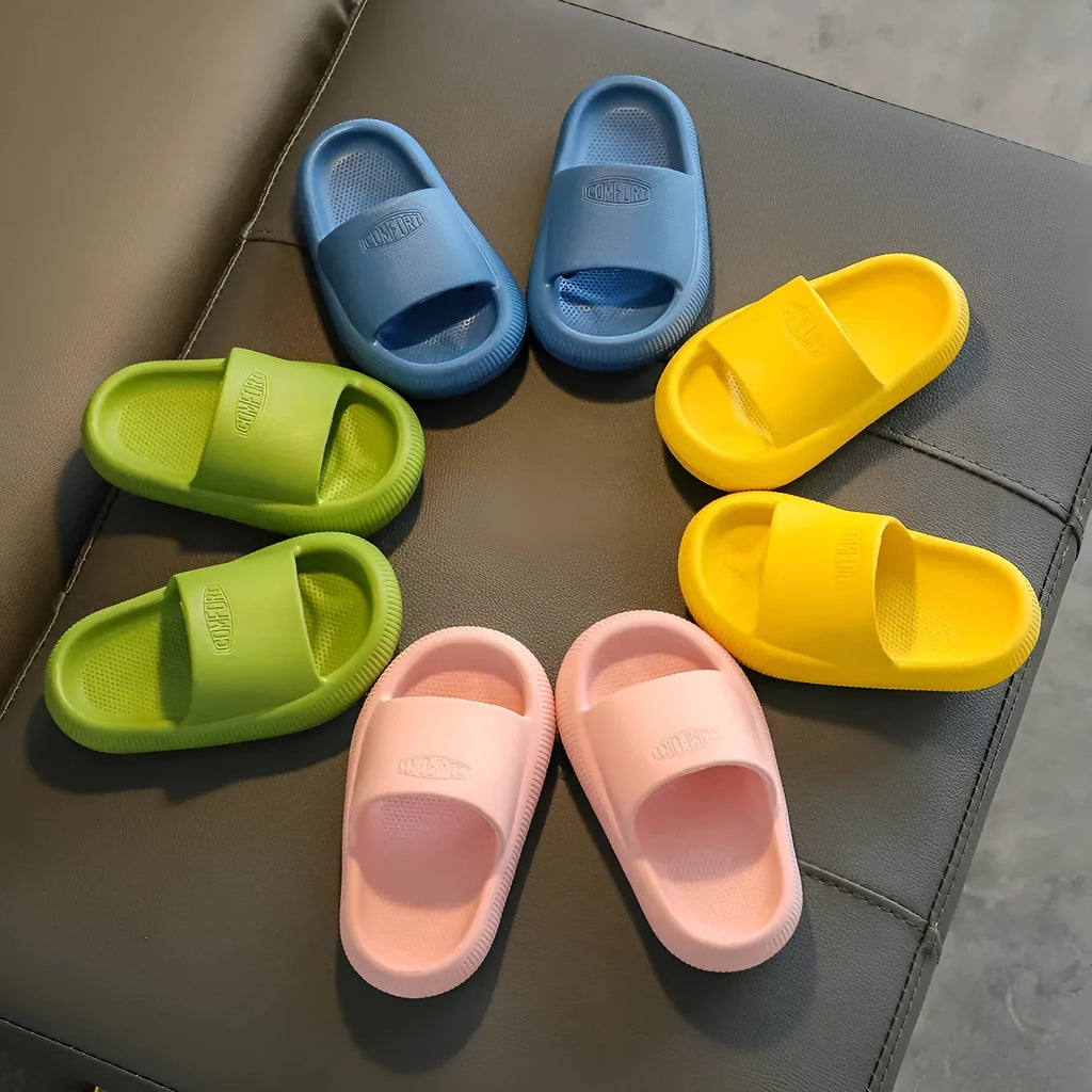 Bright coloured EVA children's house slippers with thick, textured non-slip soles on a wooden floor.