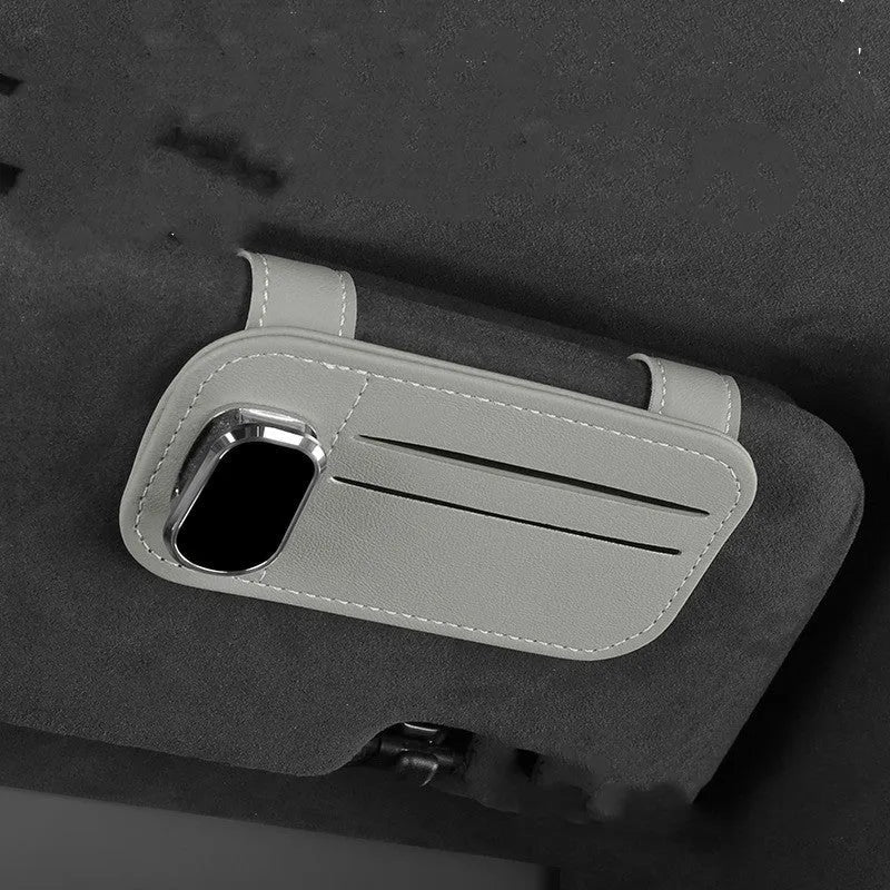 Beige cowhide automotive sun visor clip holding cards and sunglasses.