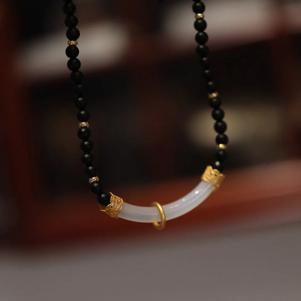 Close-up of a Chinese style U-shaped necklace with a frosted black agate and white chalcedony pendant on a silver ball bead chain.
