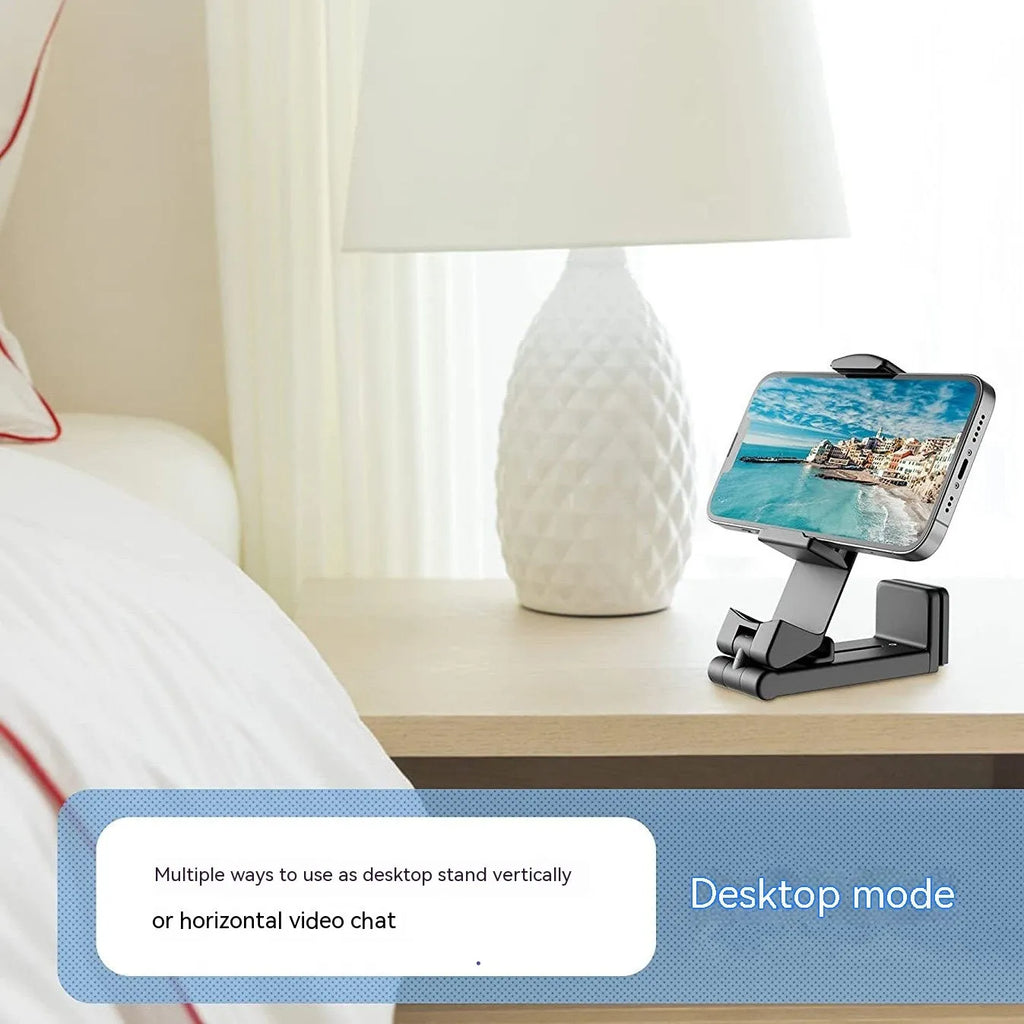 A black foldable rotating lazy phone holder gripping a mobile smartphone on a desk.