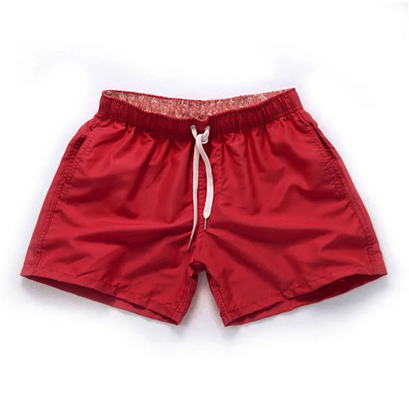 Men's straight-leg polyester surf shorts on a beach, showing colour options like black, fluorescent yellow, and navy blue.