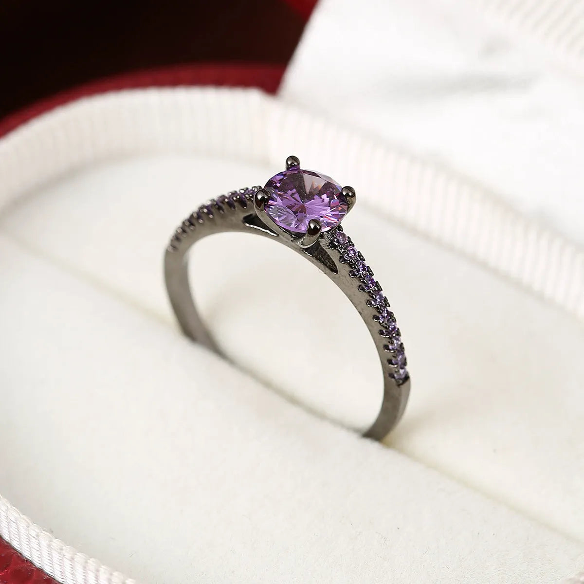 A hexagonal geometric ring with a zircon stone, shown in a gun black and rose red electroplated finish on a finger.