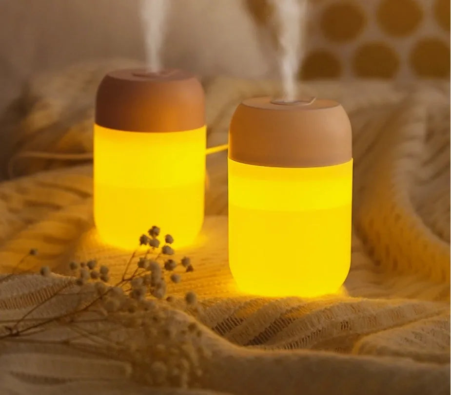 Small white cylindrical USB mini humidifier on a surface with its charging cable.