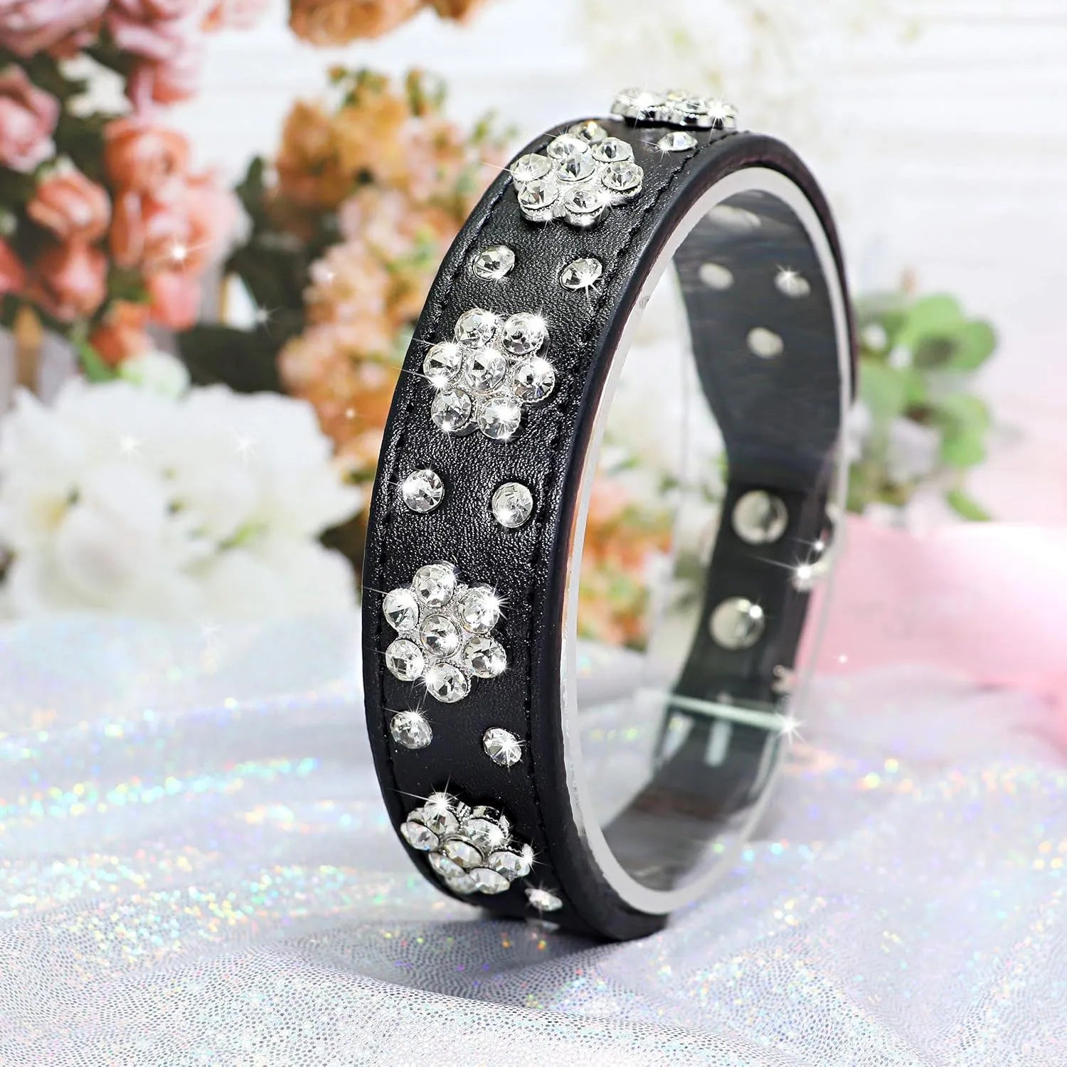 A decorative black PU leather dog collar with a sparkling rhinestone flower pattern and silver metal studs, shown adjusted with a metal D-ring.