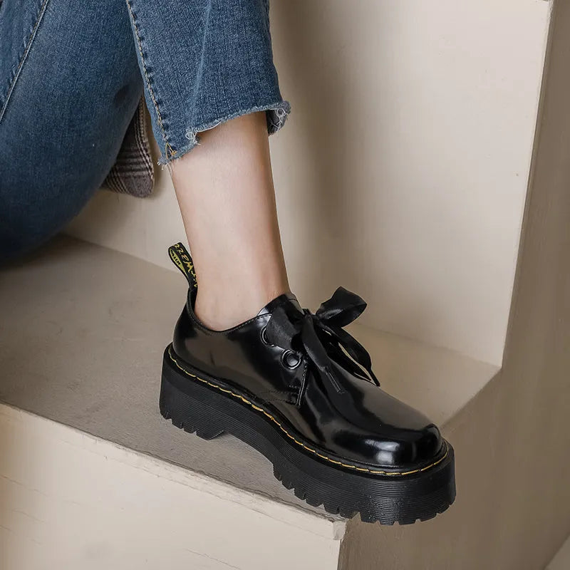 Women's black thick-soled leather shoes with ribbon and cross-strap details on a white background.
