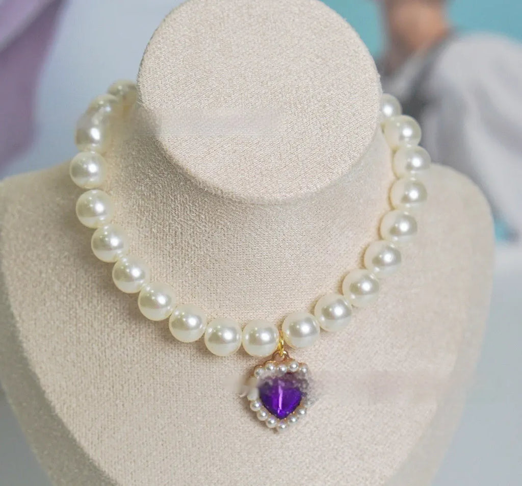 Pearl necklace cat collar with heart-shaped gem charm in various colours on a white background.