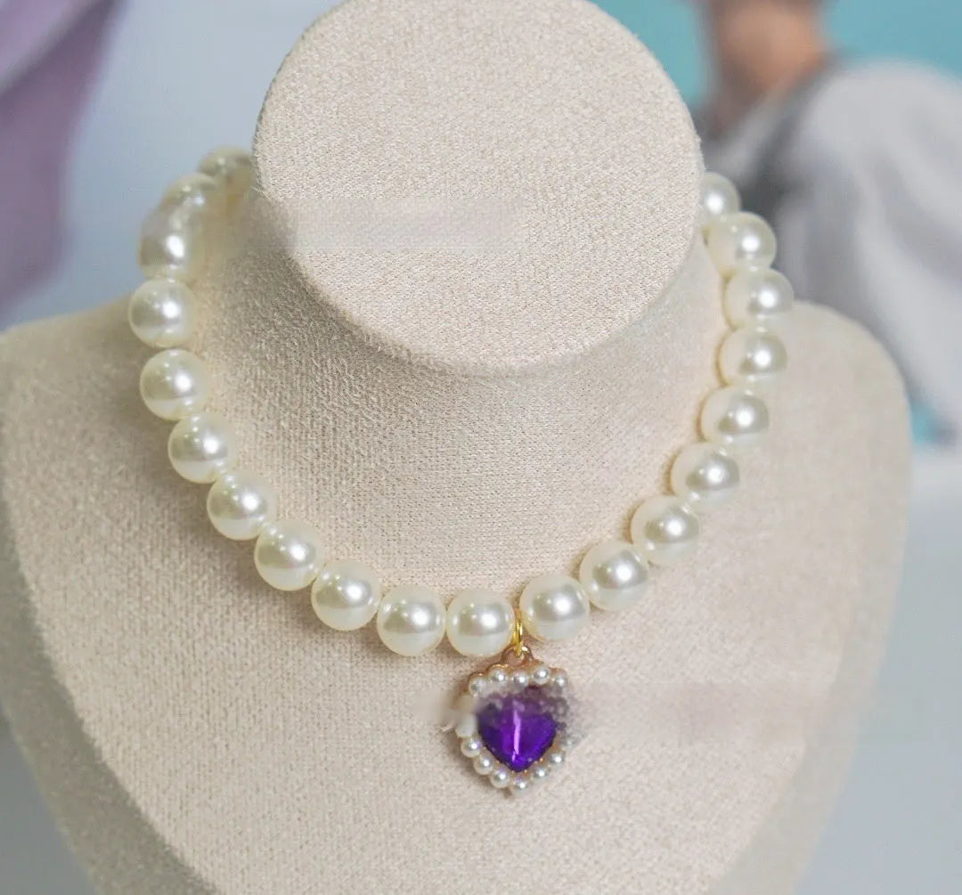 Pearl necklace cat collar with heart-shaped gem charm in various colours on a white background.