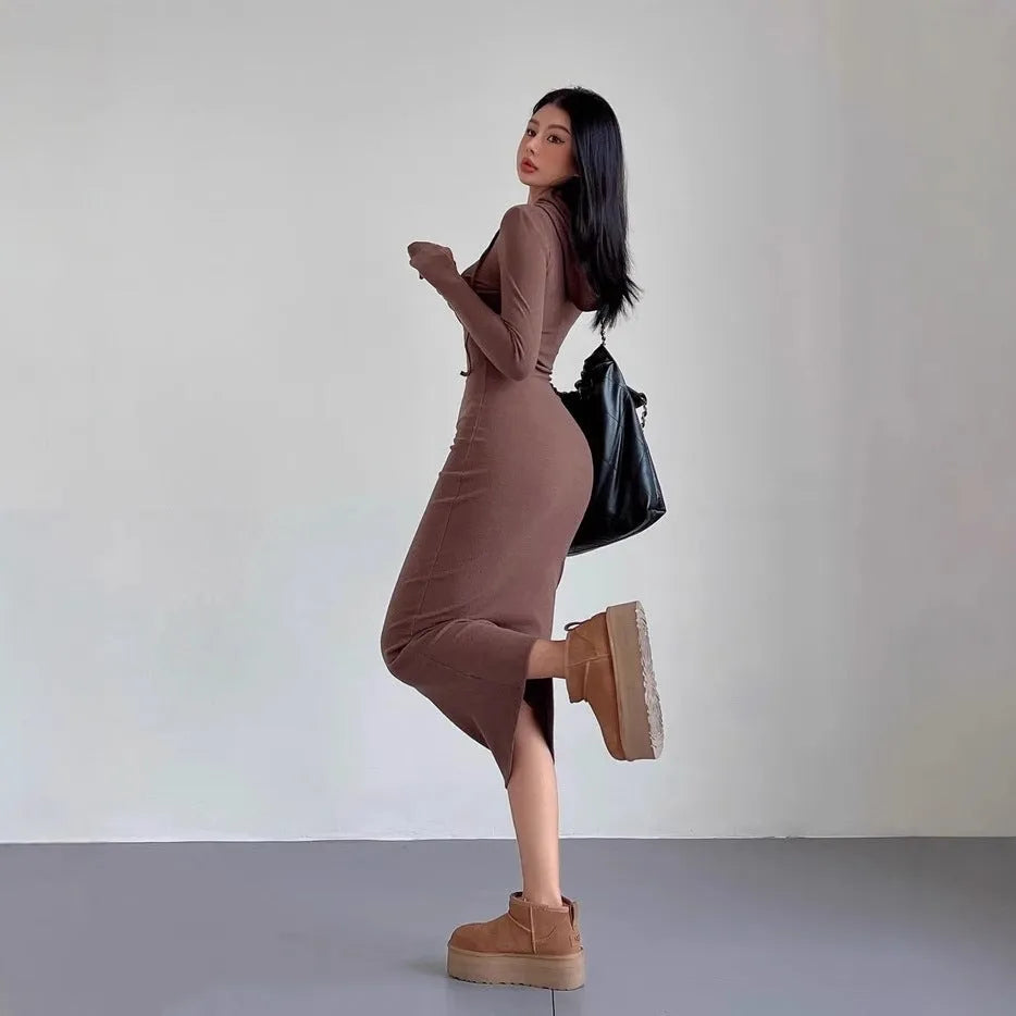 A woman modelling a grey hooded long-sleeve sheath dress with a high waist and over-the-knee length.