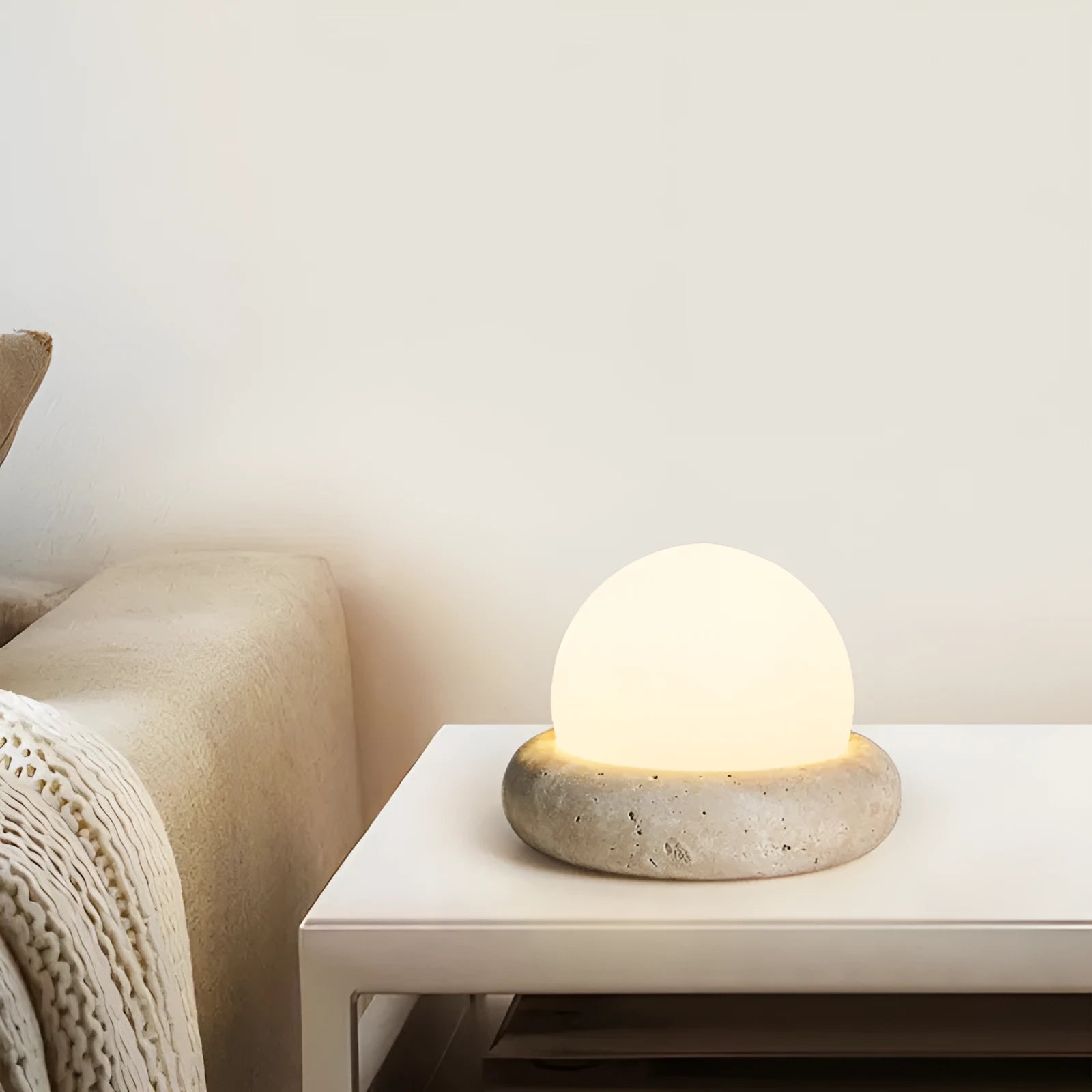 Cream coloured modern bedside night lamp with remote control on a table.