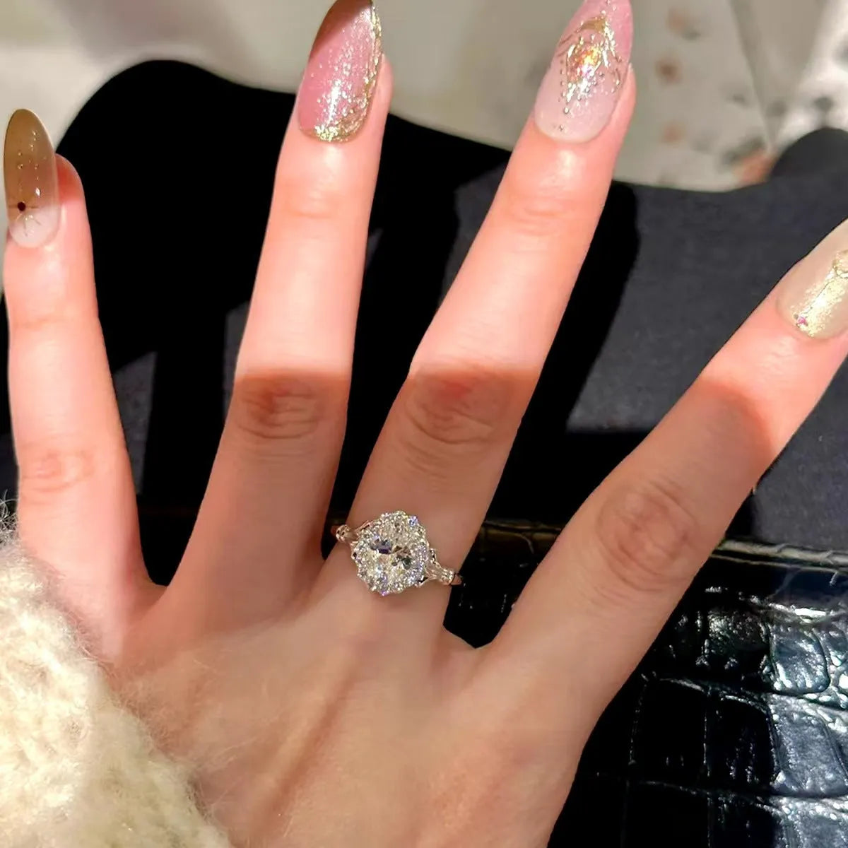 Silver geometric elliptical ring with large diamond on model's index finger, showcasing adjustable opening.