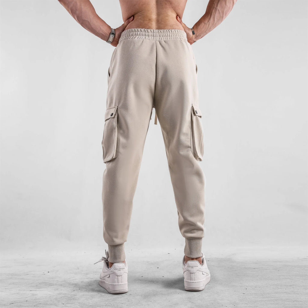 Men's loose-fit cotton sports trousers in apricot colour with ankle ties and multiple pockets, laid flat.