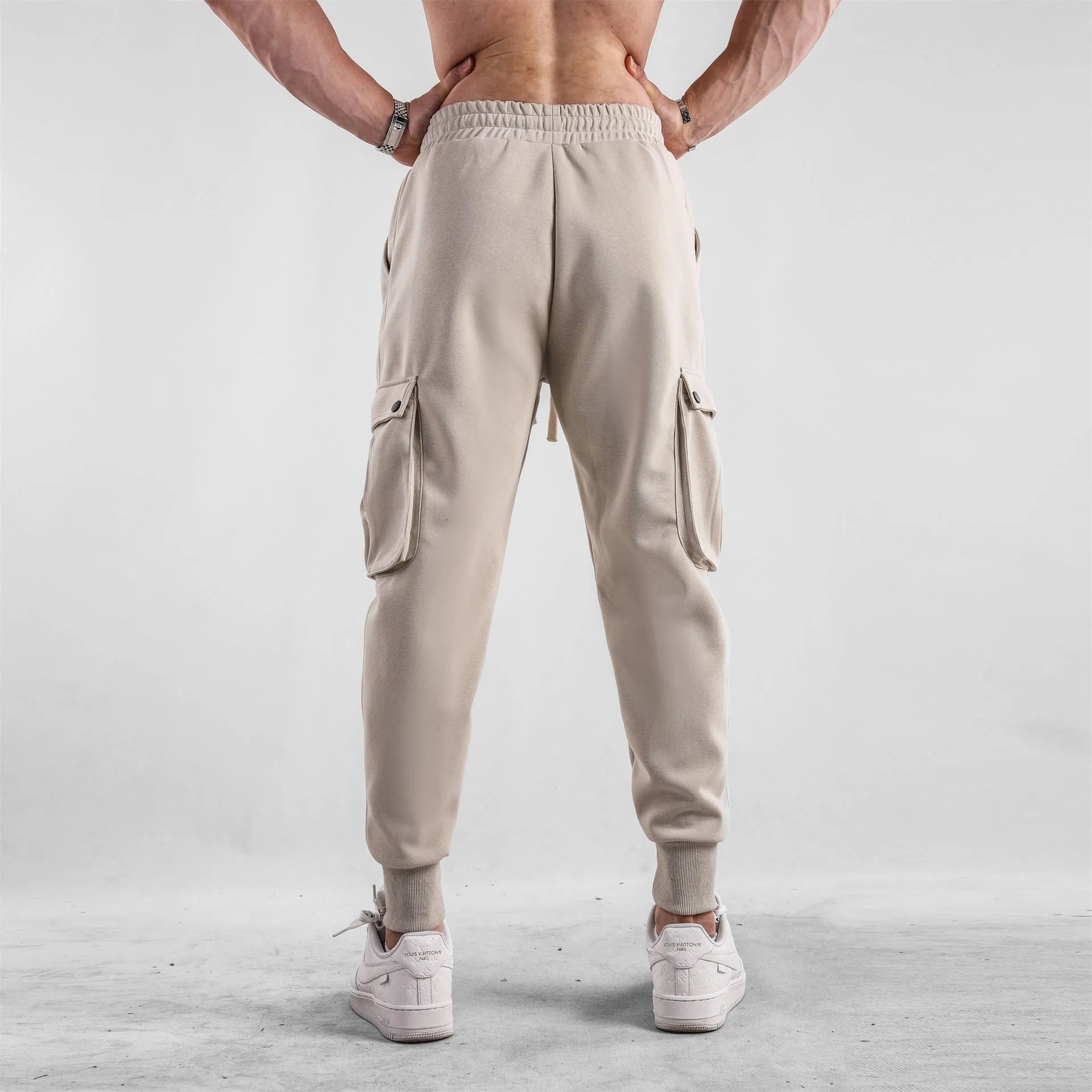 Men's loose-fit cotton sports trousers in apricot colour with ankle ties and multiple pockets, laid flat.