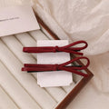 Handmade wine red leather bow hair clip on a 7cm metal alligator clip, shown on dark hair.