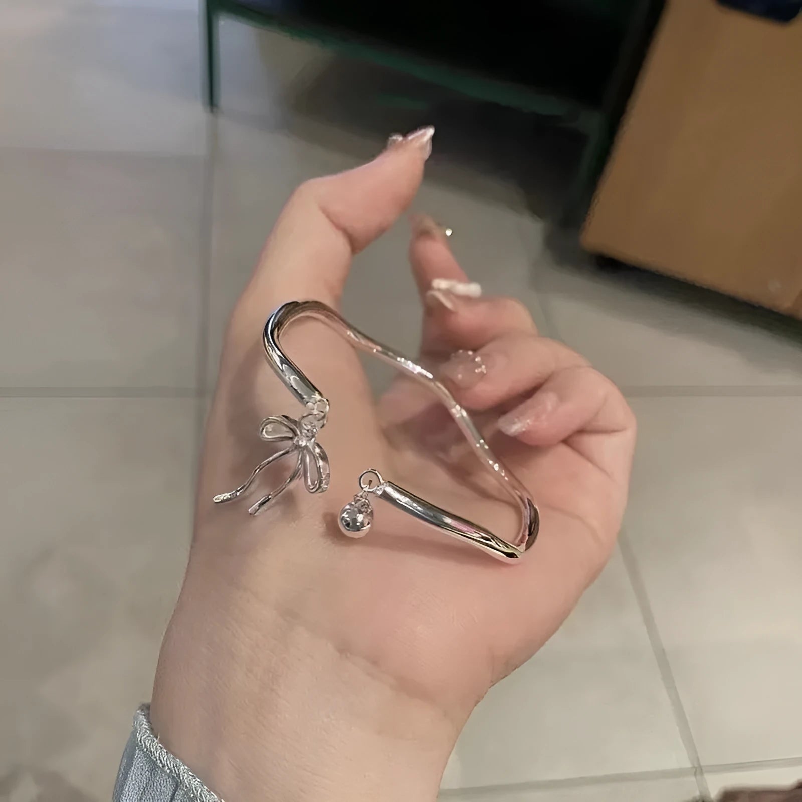 Silver adjustable bracelet with a large bow charm on a model's wrist, showing the sliding clasp.