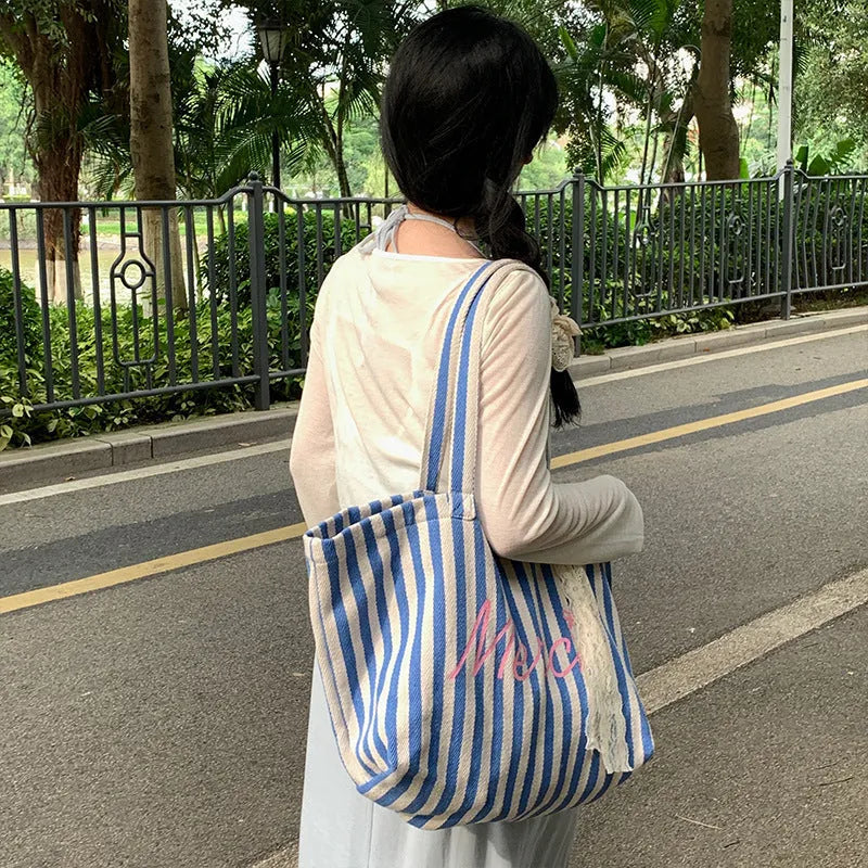 Blue striped letters printed on a pink, blue and white striped cotton canvas bag.