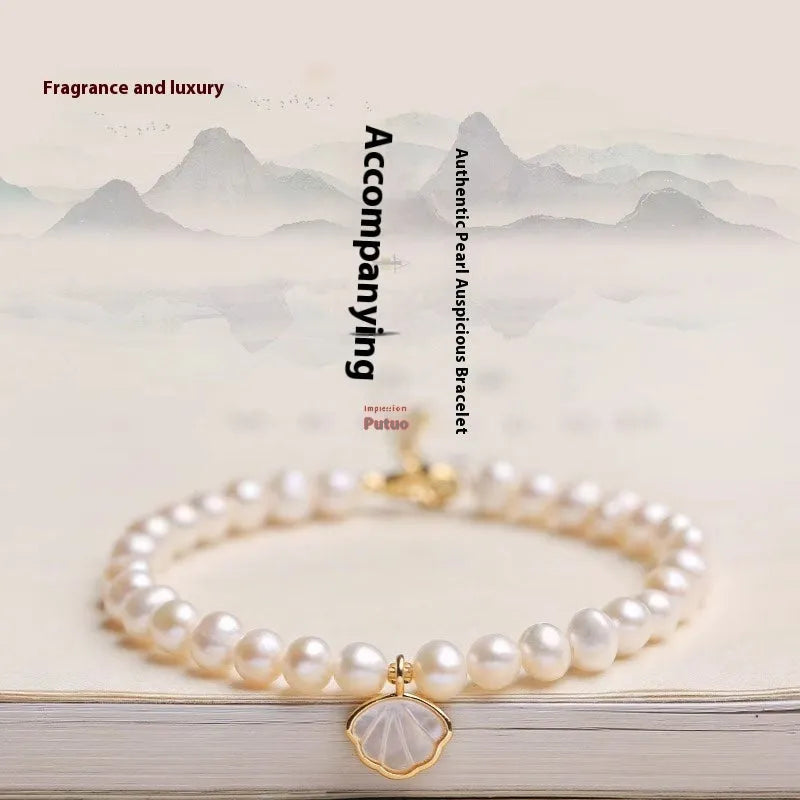 Women's freshwater pearl bracelet with a fan-shaped shell clasp on a wrist.