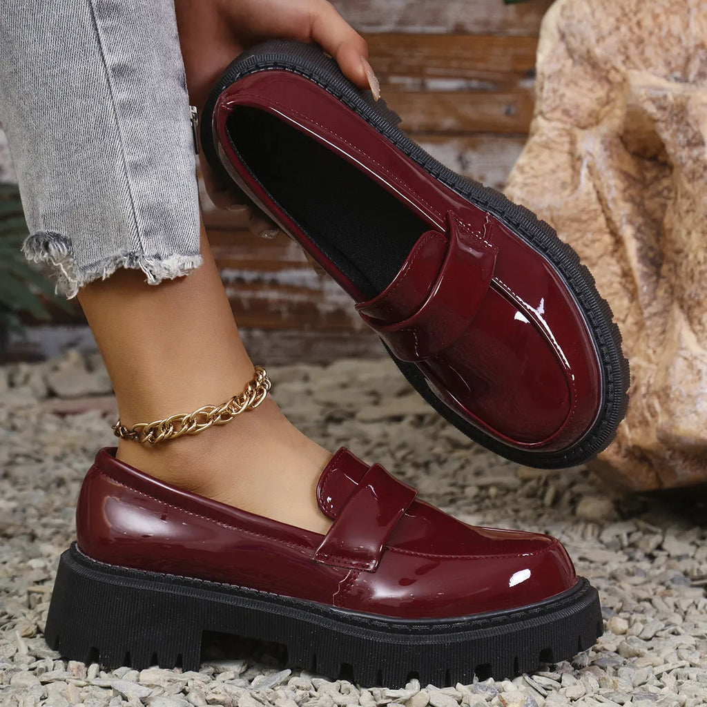 Black British style slip-on loafers with a chunky platform heel and thick rubber sole on a plain background.