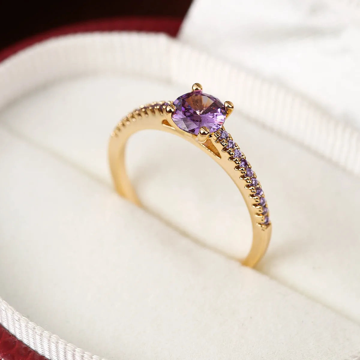 A hexagonal geometric ring with a zircon stone, shown in a gun black and rose red electroplated finish on a finger.