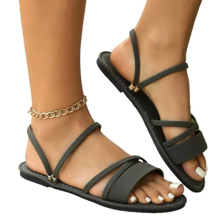 Plus-size women's sandals with a black flip-toe buckle and cross-strap on a flat rubber sole.