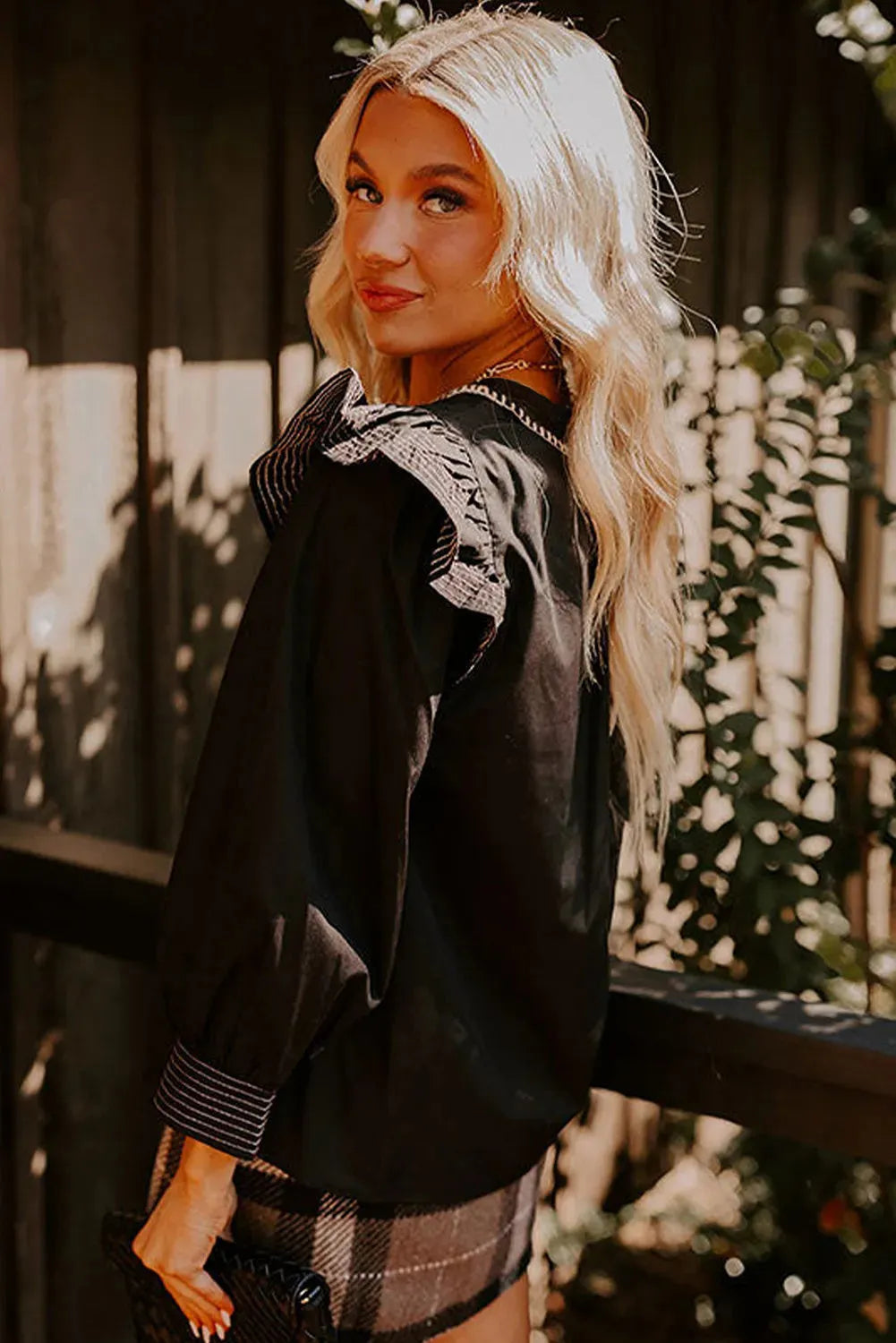 Black women's V-neck long sleeve blouse with ruffle trim and contrast stitching detail.