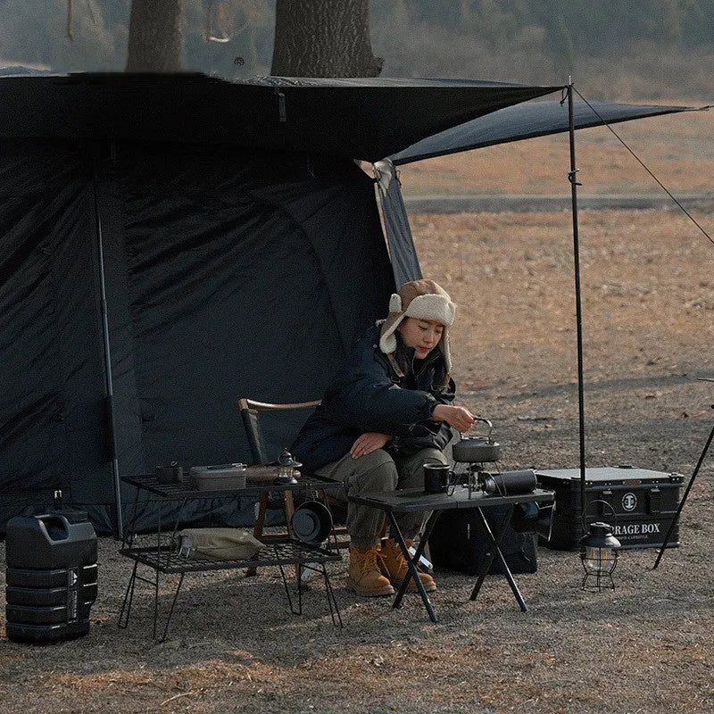 Black folding outdoor camping table with steel frame and storage bag on a campsite