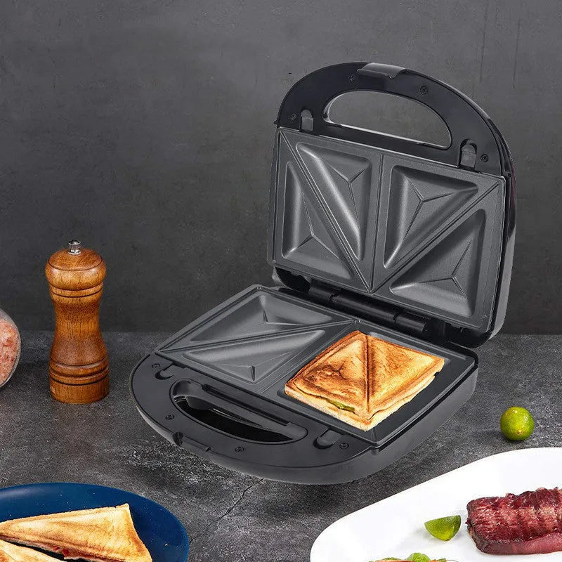 Black electric sandwich pan with brushed stainless steel lid and six non-stick cooking plates on a kitchen counter.