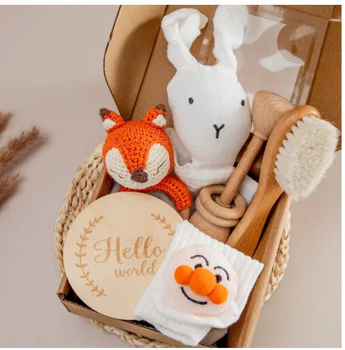 Baby teething toy gift set showing gauze blanket, wooden bell, gum teether, tire brush, and milestone on white background