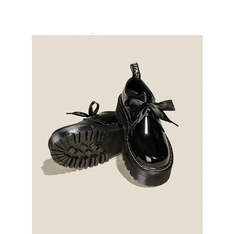 Women's black thick-soled leather shoes with ribbon and cross-strap details on a white background.