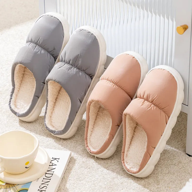 A pair of blue down cotton winter slippers with a thick rubber sole and plush lining on a wooden floor.